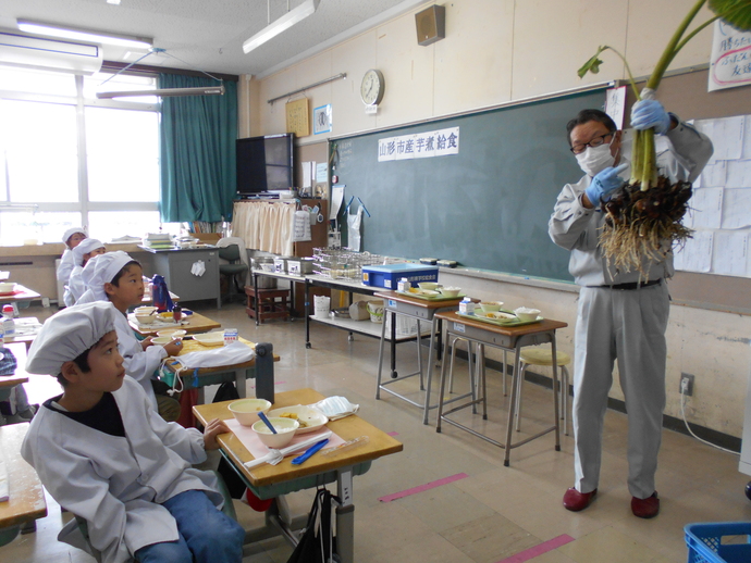 生産農家さんが児童に里いもの実物を見せている写真