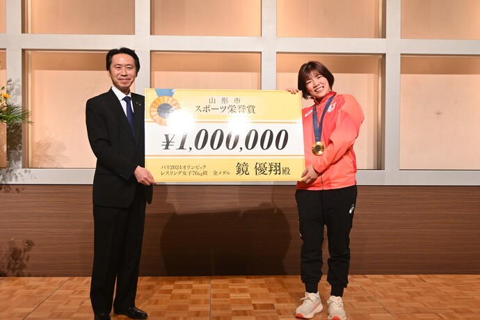 副賞の100万円のレプリカを掲げる鏡選手と佐藤市長