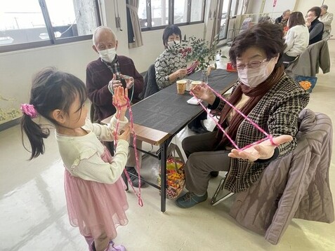 住民同士（子どもと高齢者）があやとりをして交流している様子の写真